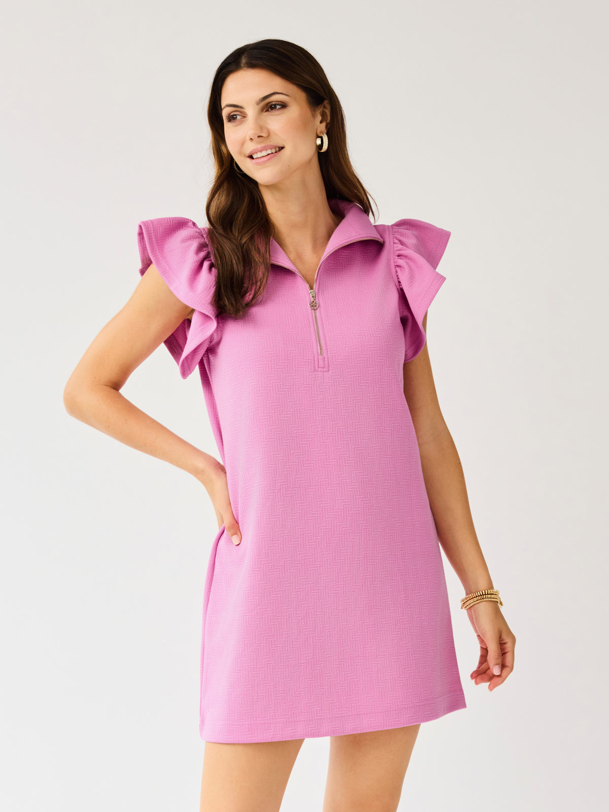 Woman wearing a pink dress with ruffled sleeves on a light gray background