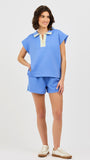 Woman wearing a blue two piece matching set with a white and gold zipper on a light gray background
