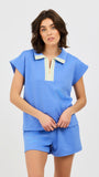 Woman wearing a blue two piece matching set with a white and gold zipper on a light gray background