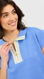 Woman wearing a blue two piece matching set with a white and gold zipper on a light gray background