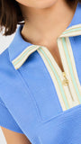 Woman wearing a blue two piece matching set with a white and gold zipper on a light gray background