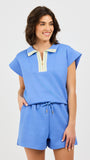 Woman wearing a blue two piece matching set with a white and gold zipper on a light gray background