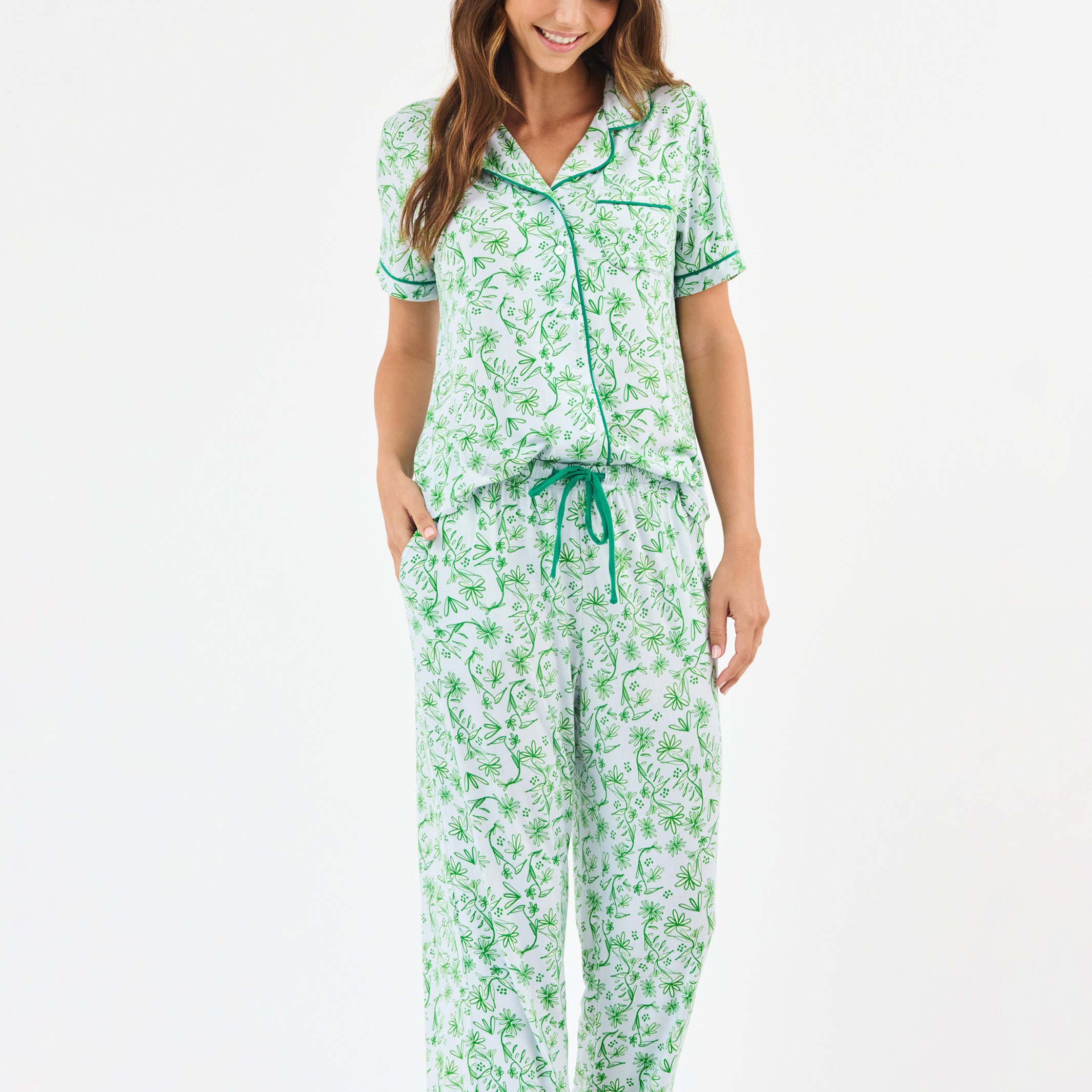 Woman wearing a green floral two piece pajama set with collar on a white background