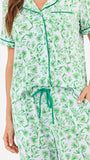 Woman wearing a green floral two piece pajama set with collar on a white background