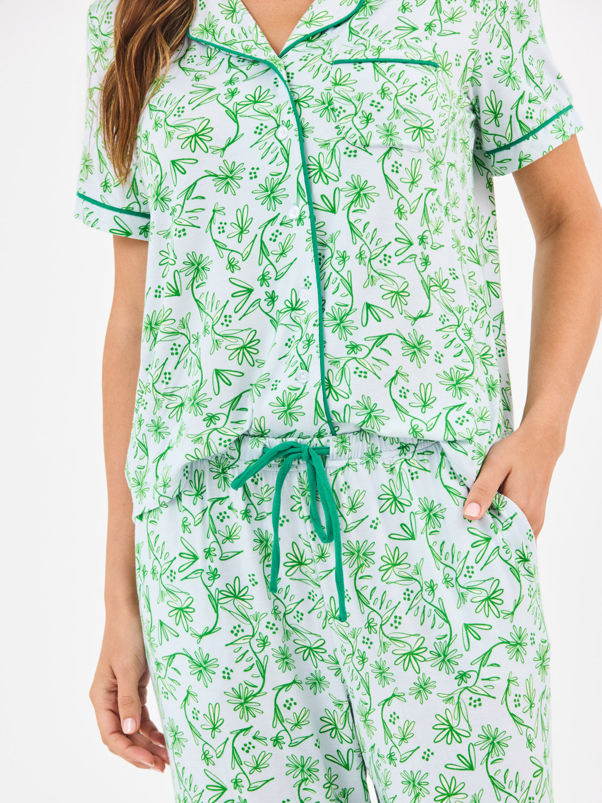 Woman wearing a green floral two piece pajama set with collar on a white background