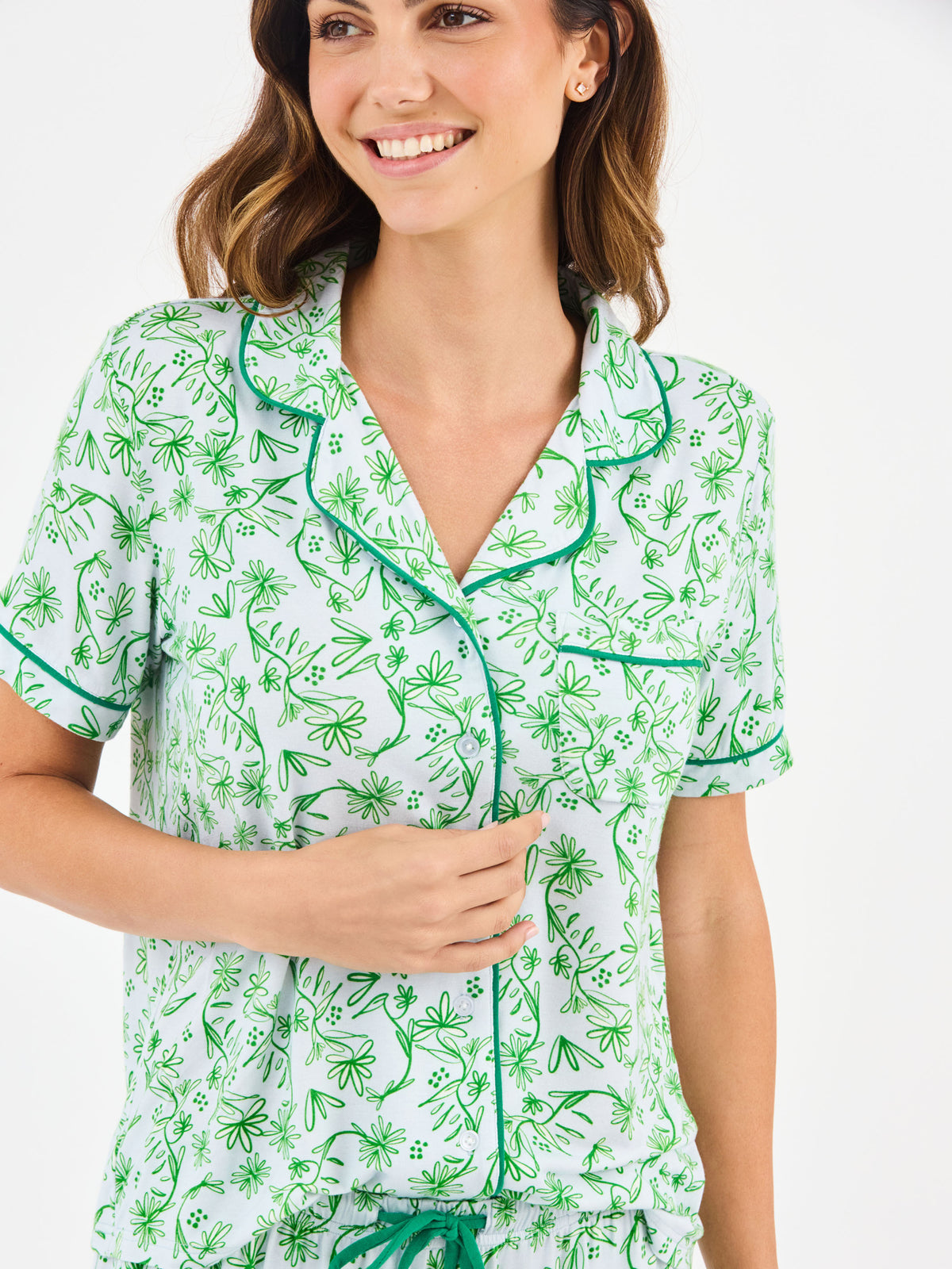 Woman wearing a green floral two piece pajama set with collar on a white background