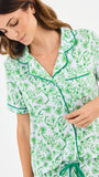 Woman wearing a green floral two piece pajama set with collar on a white background
