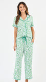 Woman wearing a green floral two piece pajama set with collar on a white background