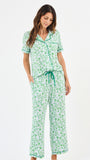 Woman wearing a green floral two piece pajama set with collar on a white background