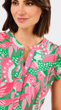 Woman wearing a colorful patterned top with pink parrots and green background