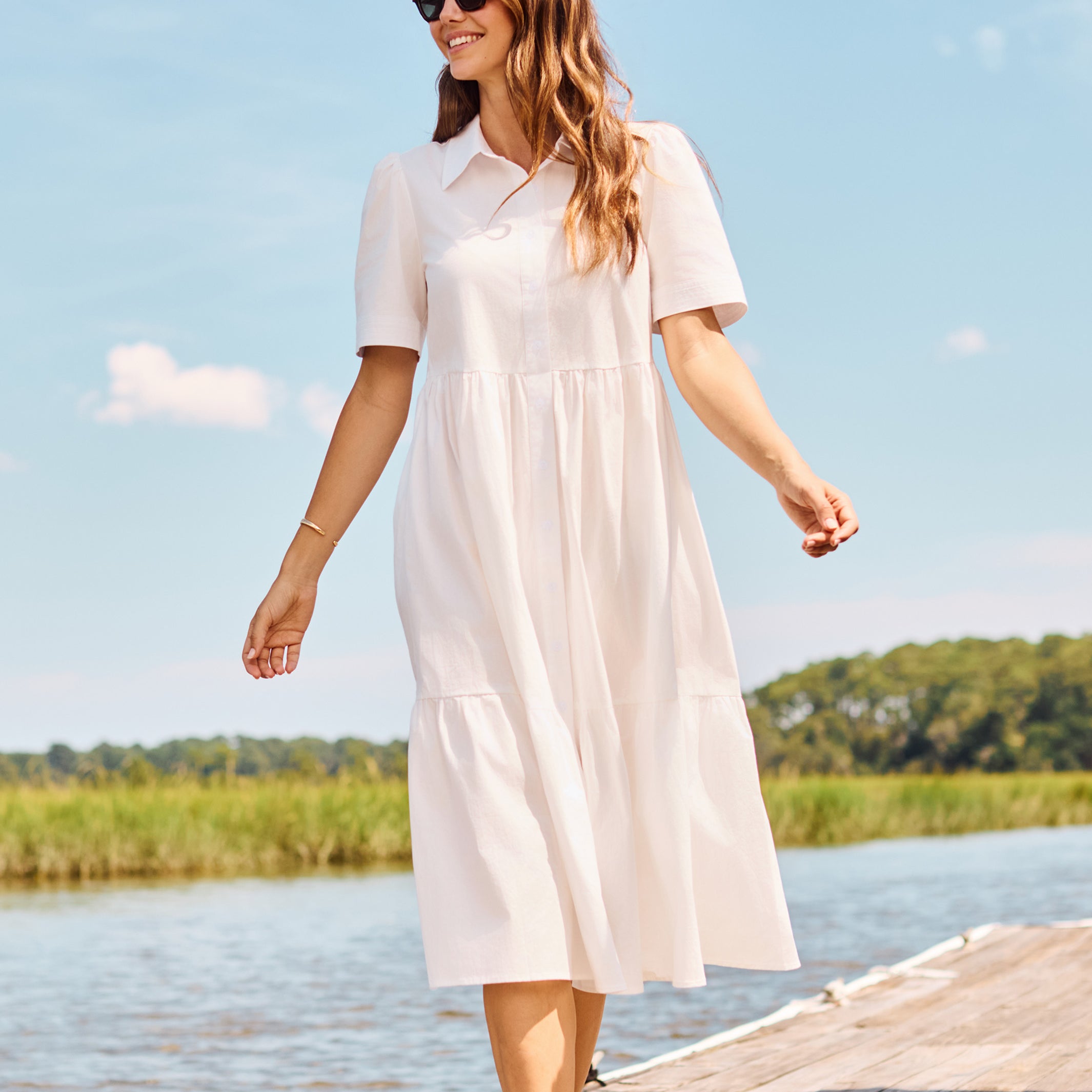 Woman in a white dress walking on a dock by a lake