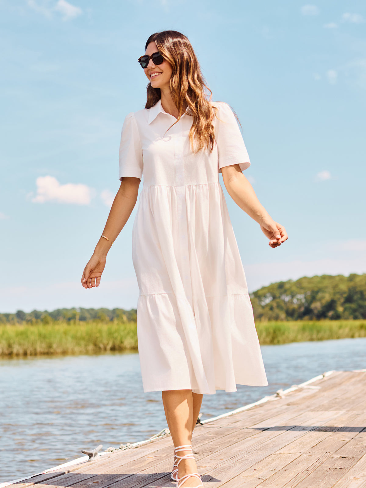 Woman in a white dress walking on a dock by a lake