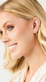 Close-up of a woman with blonde hair and blue eyes, wearing earrings on a light background