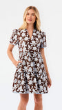 A woman modeling a short-sleeve brown and blue and white floral print dress against a plain white studio background.