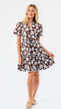A woman modeling a short-sleeve brown and blue and white floral print dress against a plain white studio background.