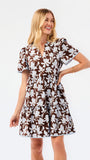 A woman modeling a short-sleeve brown and blue and white floral print dress against a plain white studio background.