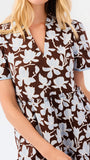 A woman modeling a short-sleeve brown and blue and white floral print dress against a plain white studio background.