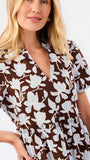A woman modeling a short-sleeve brown and blue and white floral print dress against a plain white studio background.