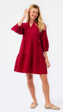 A woman modeling a tiered red dress with three-quarter puff sleeves and a V-neckline, paired with beige woven flat shoes, against a plain white studio background.