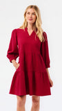 A woman modeling a tiered red dress with three-quarter puff sleeves and a V-neckline, photographed against a plain white studio background.