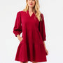 A woman modeling a tiered red dress with three-quarter puff sleeves and a V-neckline, photographed against a plain white studio background.