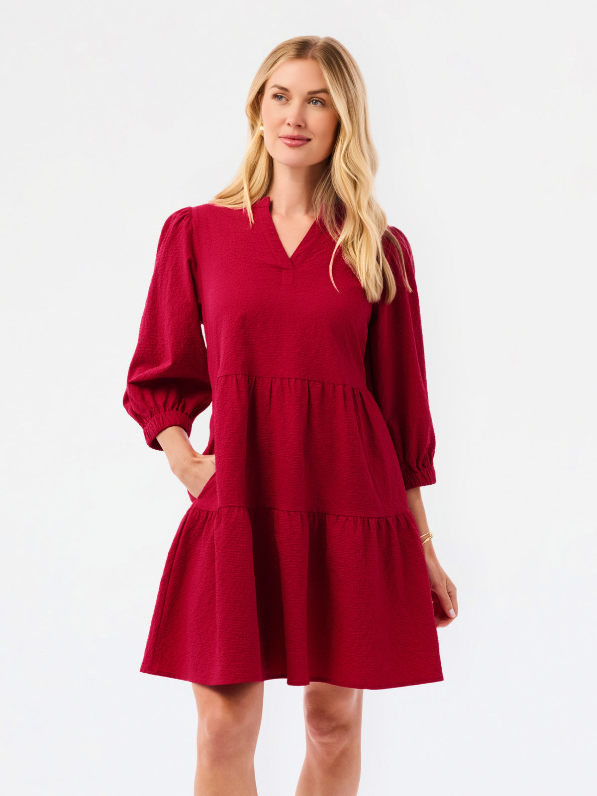 A woman modeling a tiered red dress with three-quarter puff sleeves and a V-neckline, photographed against a plain white studio background.