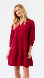 A woman modeling a tiered red dress with three-quarter sleeves and a V-neckline, photographed against a plain white studio background.