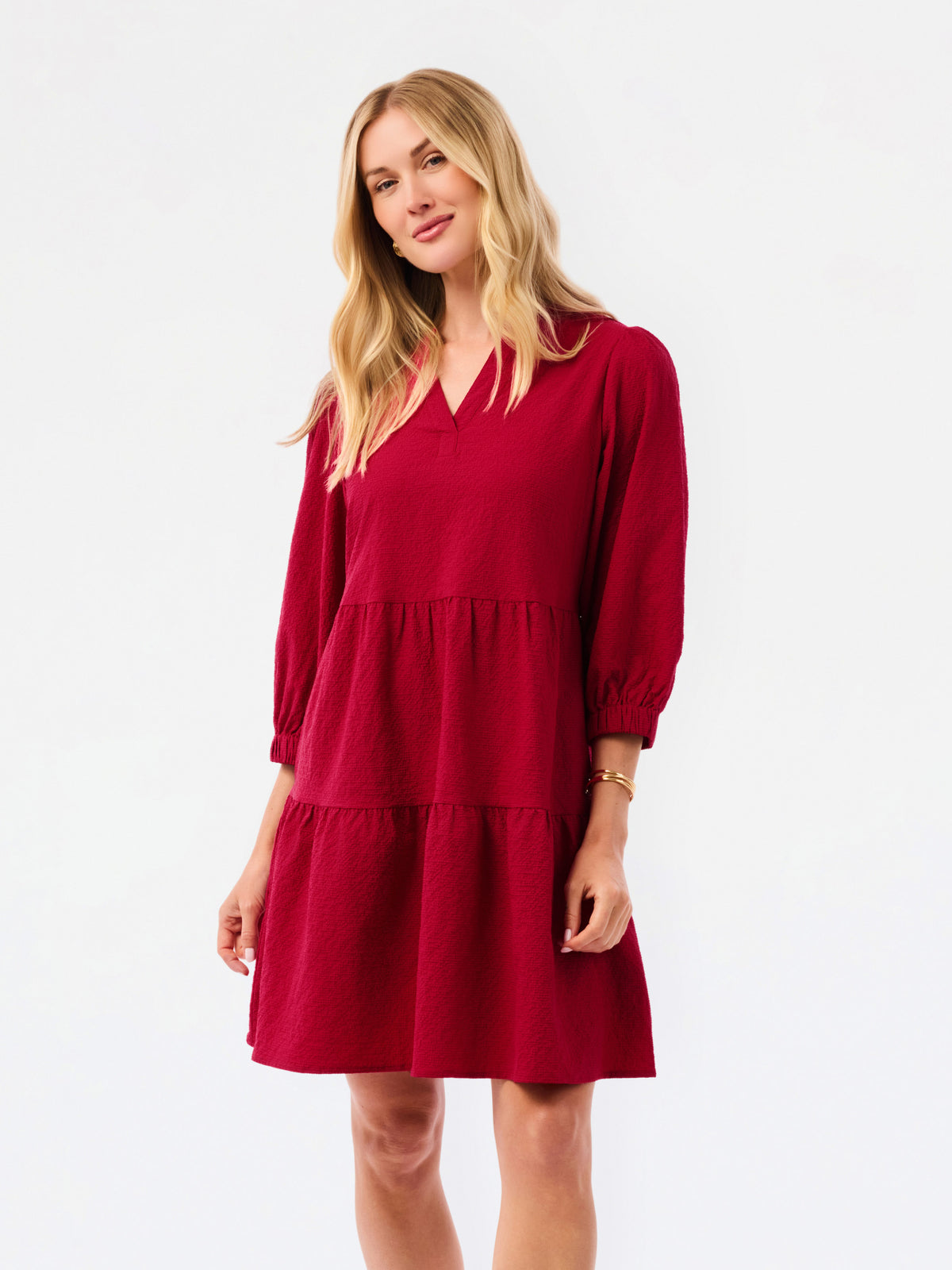 A woman modeling a tiered red dress with three-quarter sleeves and a V-neckline, photographed against a plain white studio background.