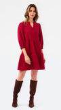 A woman modeling a short tiered red dress with three-quarter sleeves and brown knee-high boots, standing against a plain white studio background.