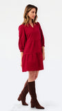 A woman modeling a red tiered mini dress with three-quarter puff sleeves, paired with dark brown knee-high boots, against a plain white studio background.