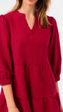A woman wearing a tiered red dress with three-quarter puff sleeves and a split neckline, shown against a plain white background.