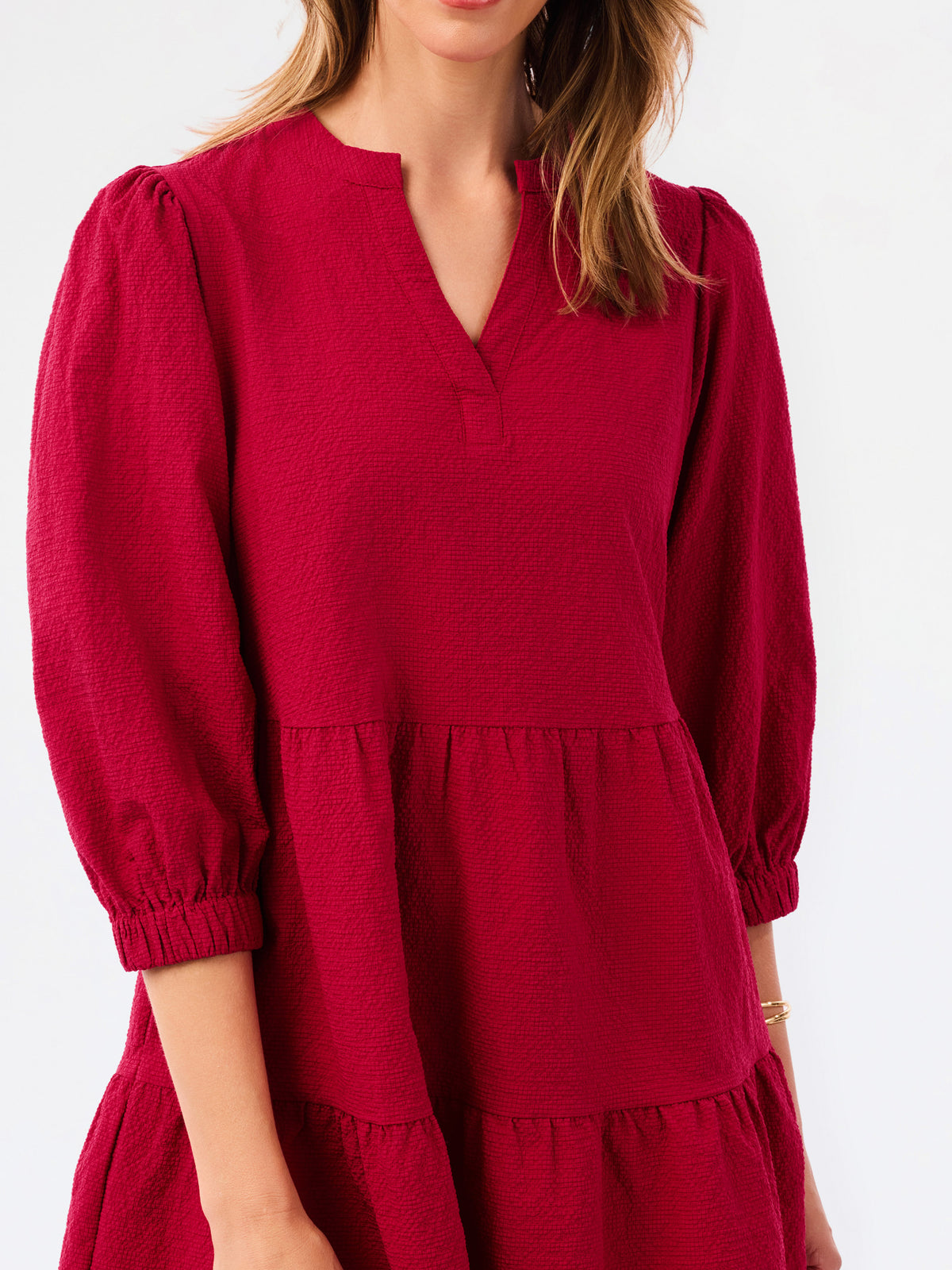 A woman wearing a tiered red dress with three-quarter puff sleeves and a split neckline, shown against a plain white background.