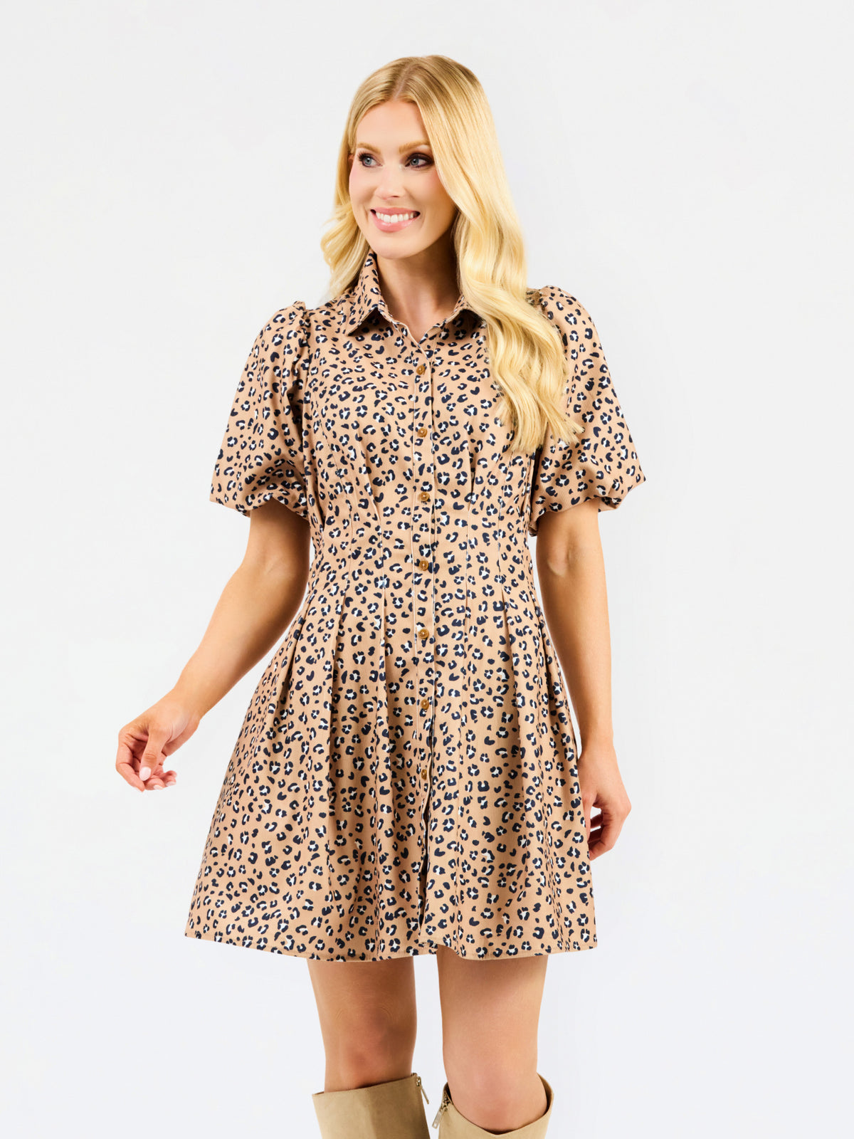 A woman modeling a short-sleeve collared dress with a beige, brown, and black leopard print pattern, set against a plain white studio background.