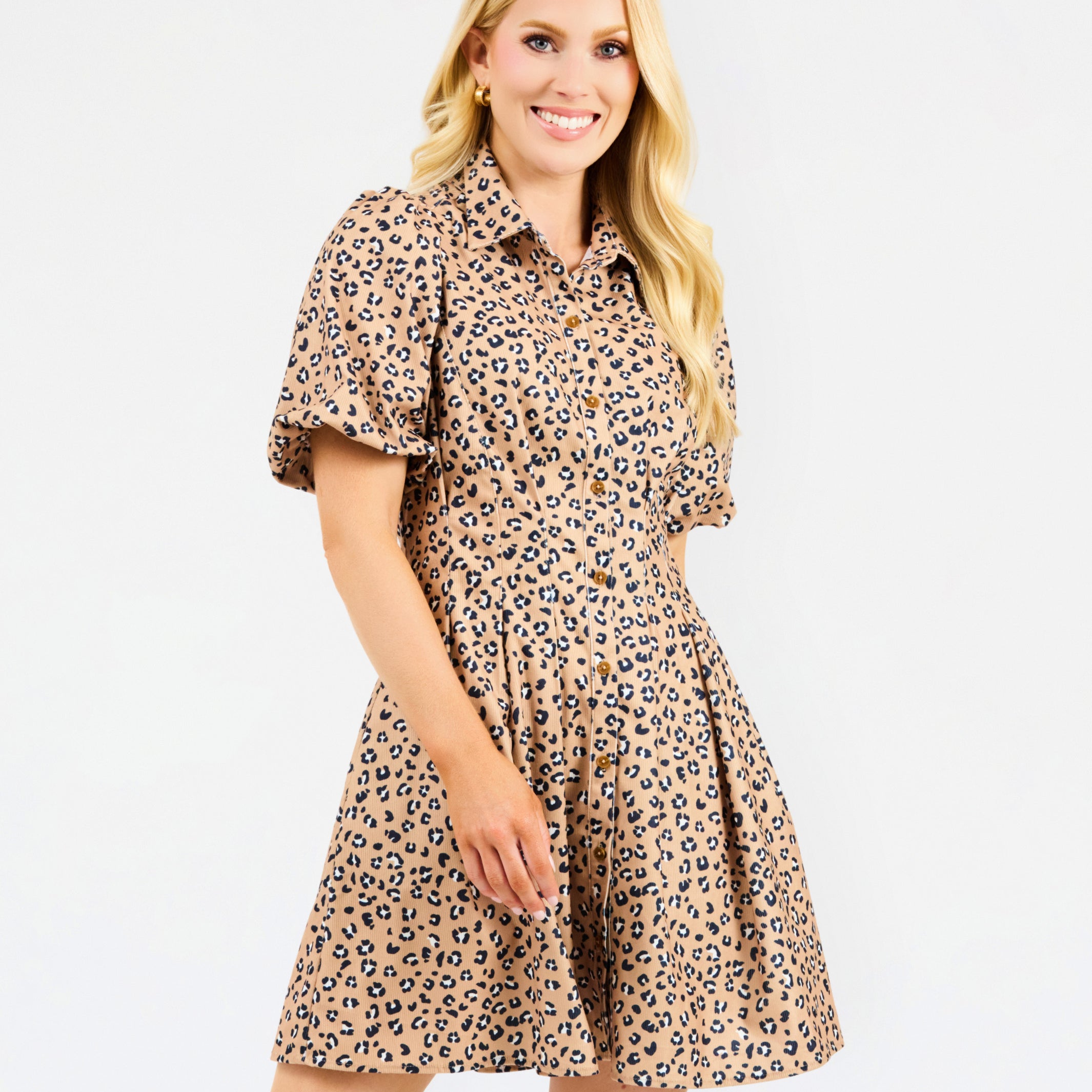 A woman modeling a short-sleeve collared dress with a beige, brown, and black leopard print pattern, set against a plain white studio background.