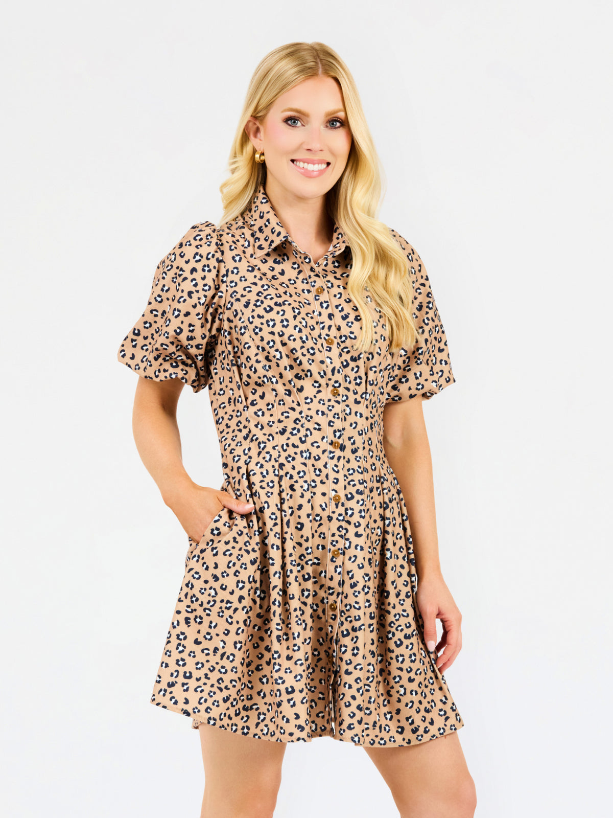 A woman modeling a short-sleeve collared dress with a beige, brown, and black leopard print pattern, set against a plain white studio background.