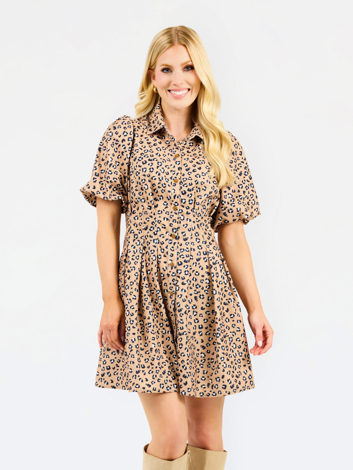 A woman modeling a short-sleeve collared dress with a beige, brown, and black leopard print pattern, set against a plain white studio background.