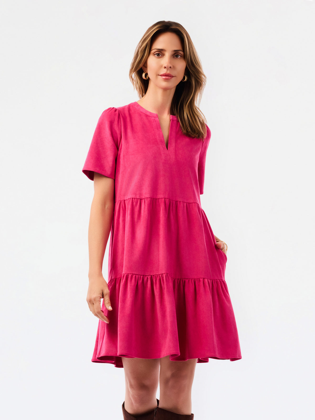 A woman modeling a bright pink tiered short-sleeve dress with a split neckline, photographed against a clean white studio background.