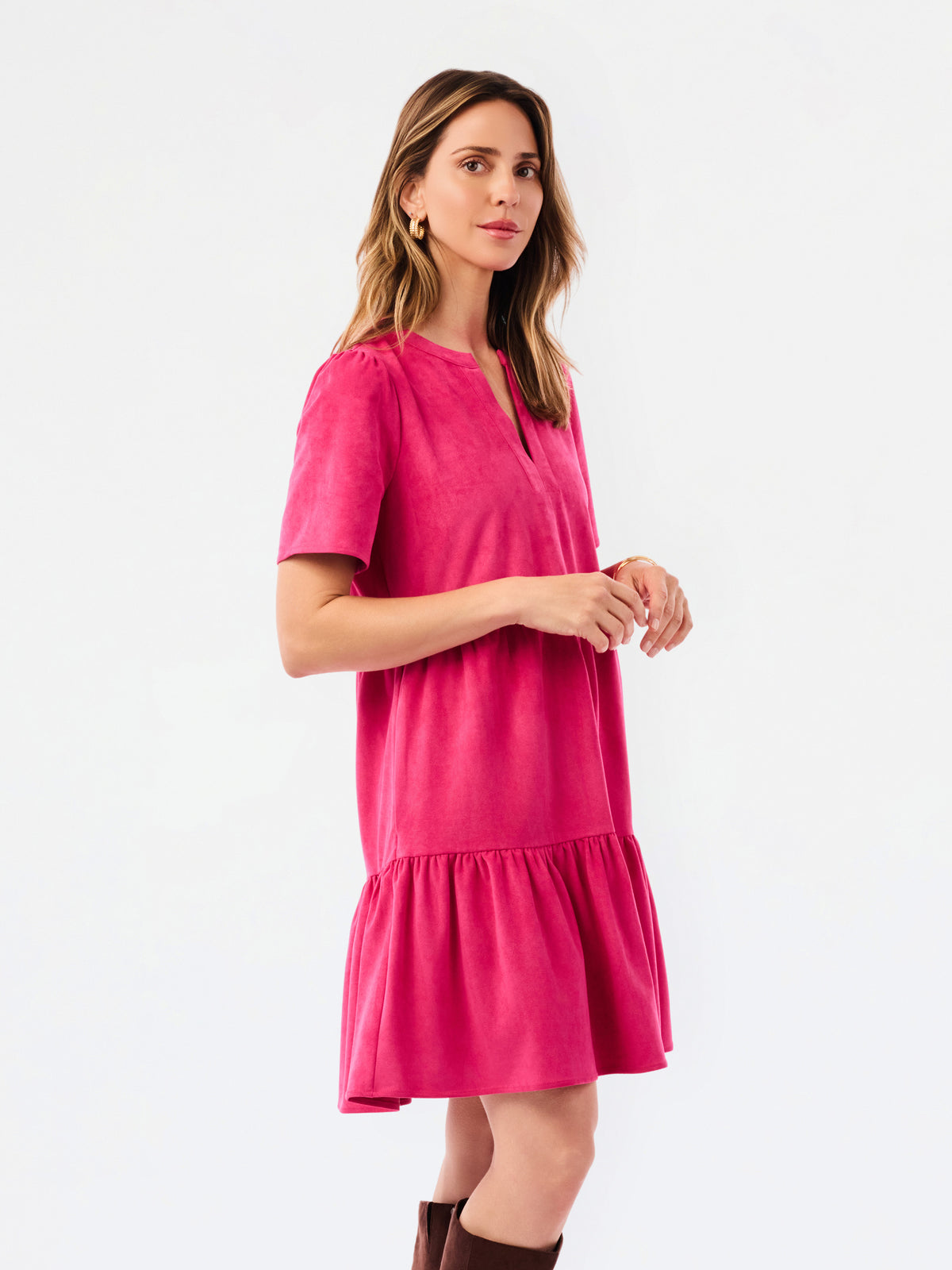 A woman modeling a short-sleeve pink tiered dress with a split neckline, paired with brown knee-high boots, against a plain white studio background.