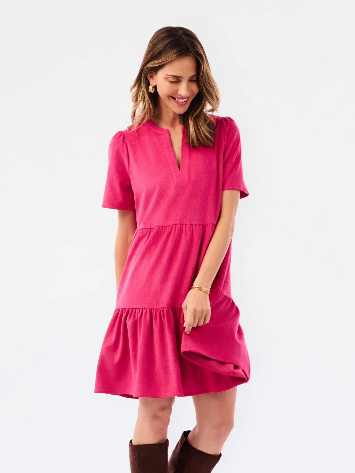 A woman modeling a bright pink tiered short-sleeve dress with a split neckline, paired with brown knee-high boots, against a plain white studio background.