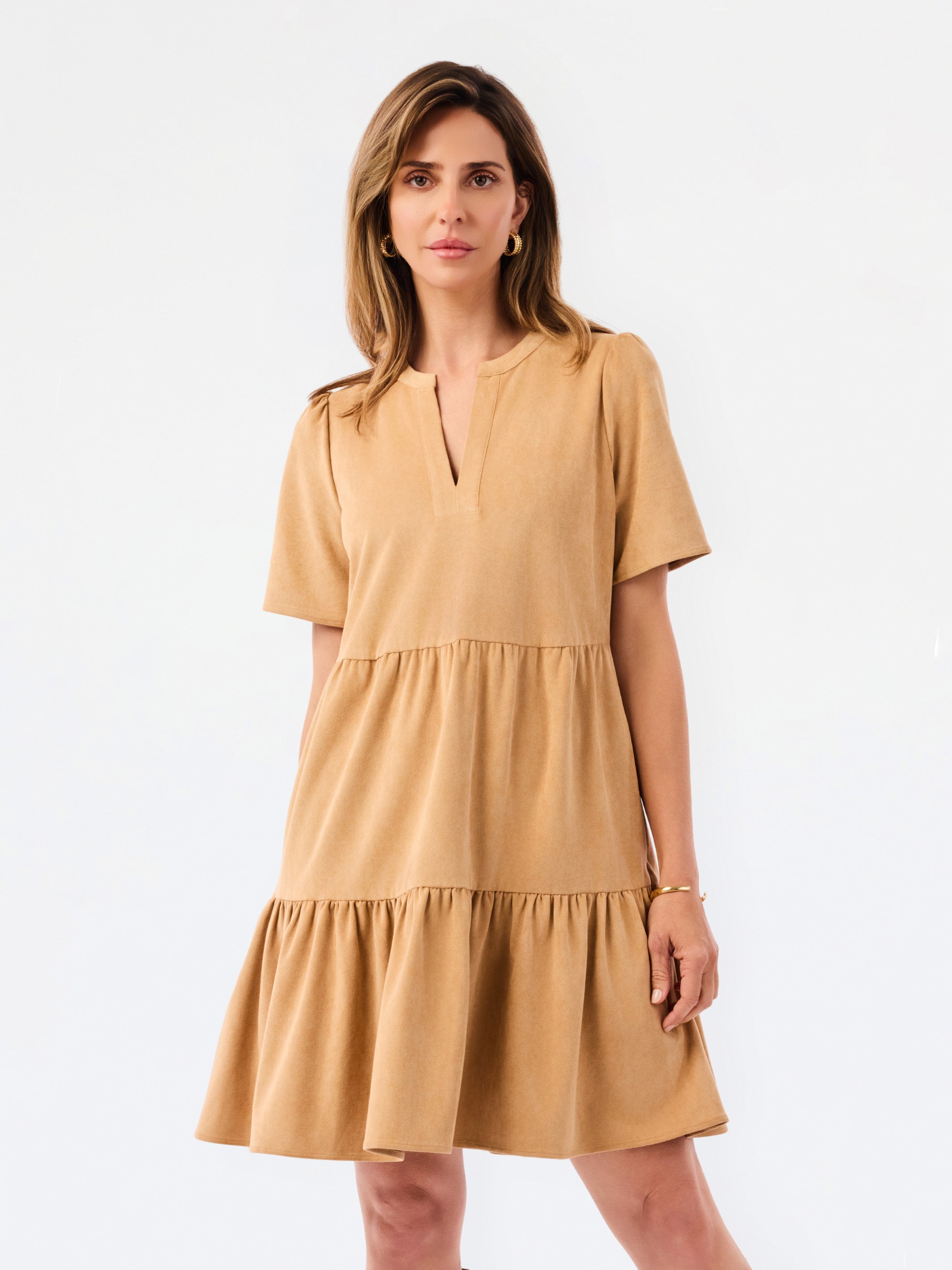 A woman modeling a short-sleeve tiered dress in a warm camel tan color, featuring a split neckline and ruffled hem, set against a plain white studio background.