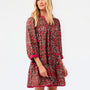 A blonde model wearing a brown short-sleeve shift dress with a red and pink floral pattern and solid pink trim, photographed against a plain white studio background.