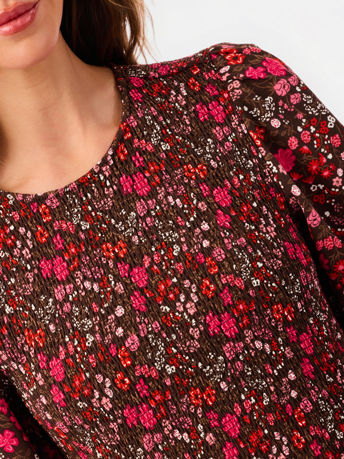 Close-up of a woman wearing a brown textured top with an all-over dense floral pattern in pink, red, and white.