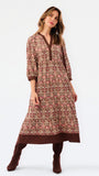 A woman modeling a long-sleeved, knee-length printed tunic dress in pink, brown, and beige, paired with matching brown boots, against a plain white studio background.