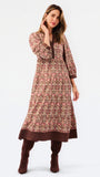 A woman modeling a long-sleeved, knee-length printed tunic dress in pink, brown, and beige, paired with matching brown boots, against a plain white studio background.