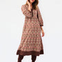 A woman modeling a long-sleeved, knee-length printed tunic dress in pink, brown, and beige, paired with matching brown boots, against a plain white studio background.