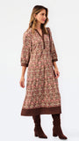 A woman modeling a long-sleeved, knee-length printed tunic dress in pink, brown, and beige, paired with matching brown boots, against a plain white studio background.