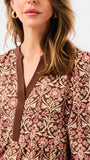 A close-up of a woman wearing a brown long-sleeve dress with a pink and beige floral pattern and a brown tie-neck detail.