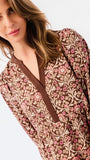 A close-up of a woman wearing a brown long-sleeve dress with a pink and beige floral damask pattern and a brown V-neckline.