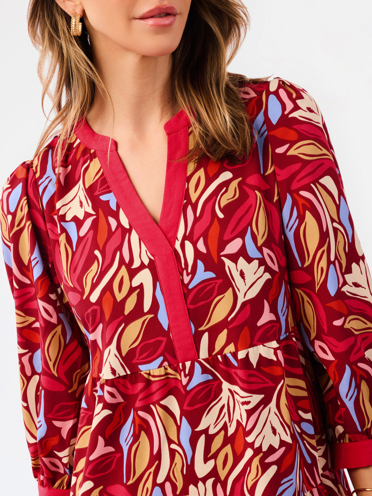 A close-up of a woman wearing a long-sleeve red dress with a bold abstract floral pattern in beige, orange, and light blue, featuring a split neckline.