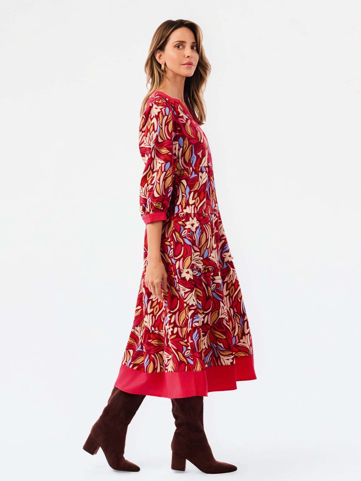 A woman modeling a red, beige, and blue abstract patterned midi dress with three-quarter sleeves and brown knee-high boots, photographed against a plain white studio background.